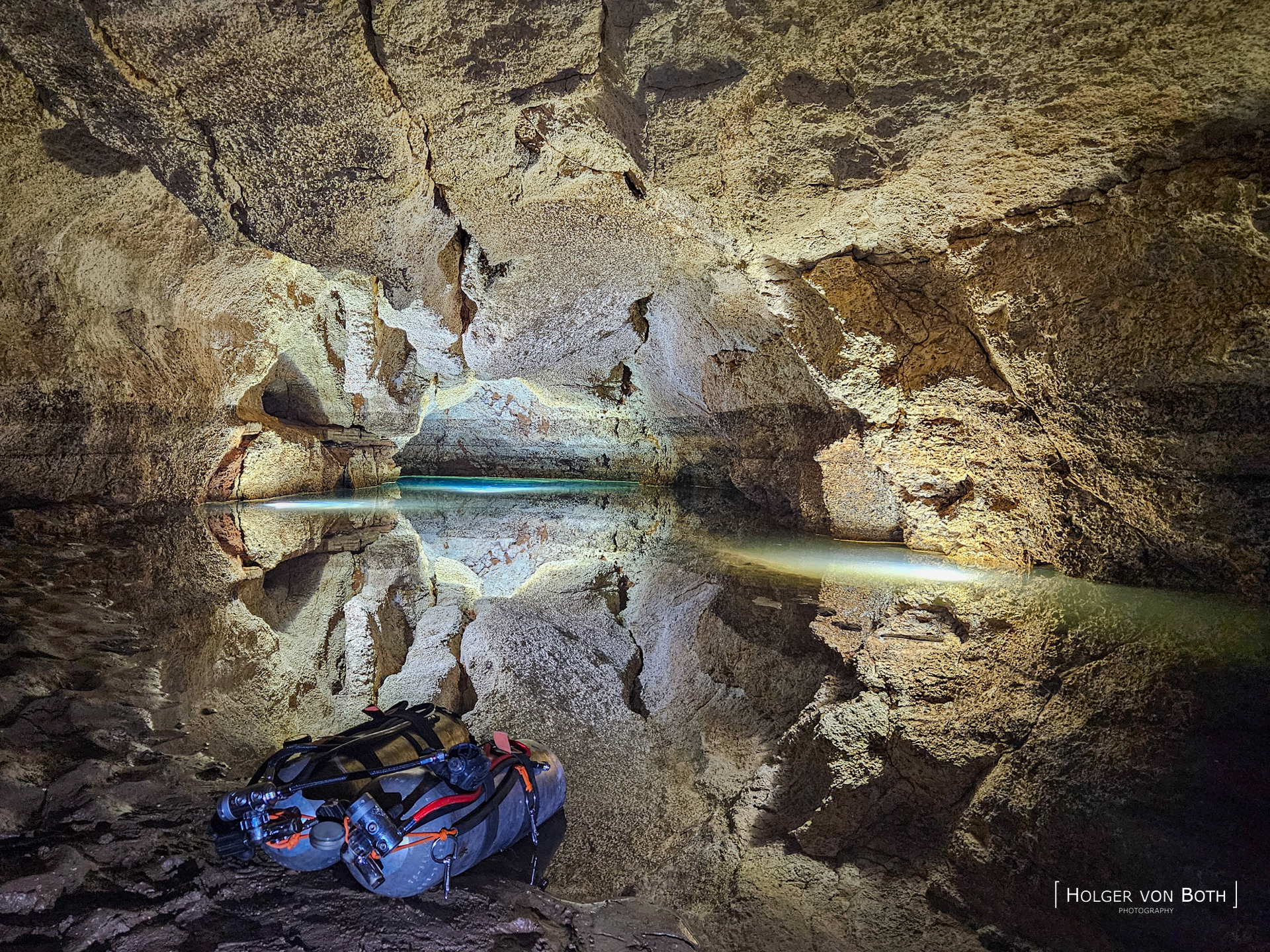 Sidemount diving tanks at the entrance of Malazamanga Cave in Madagascar with crystal clear water and reflections inside the cave.