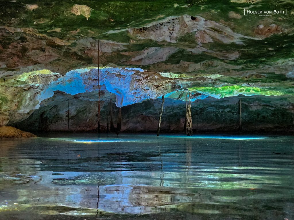 Entrance pool of Anjanamba Cave in Madagascar illuminated with dive lights beneath the limestone ceiling.