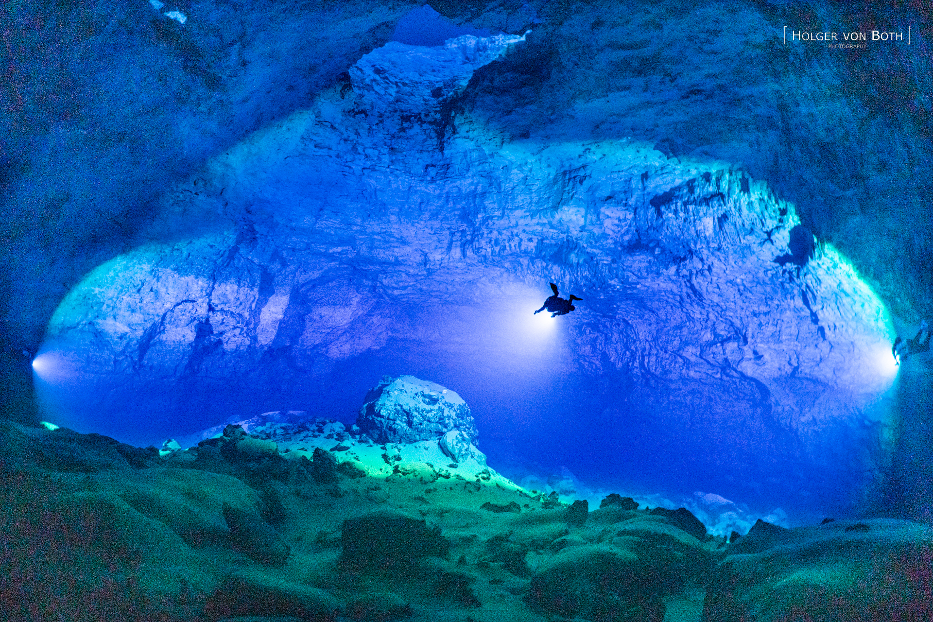 Massive underwater cave chamber in Malazamanga Cave, Madagascar, illuminated by three cave divers with powerful dive lights.