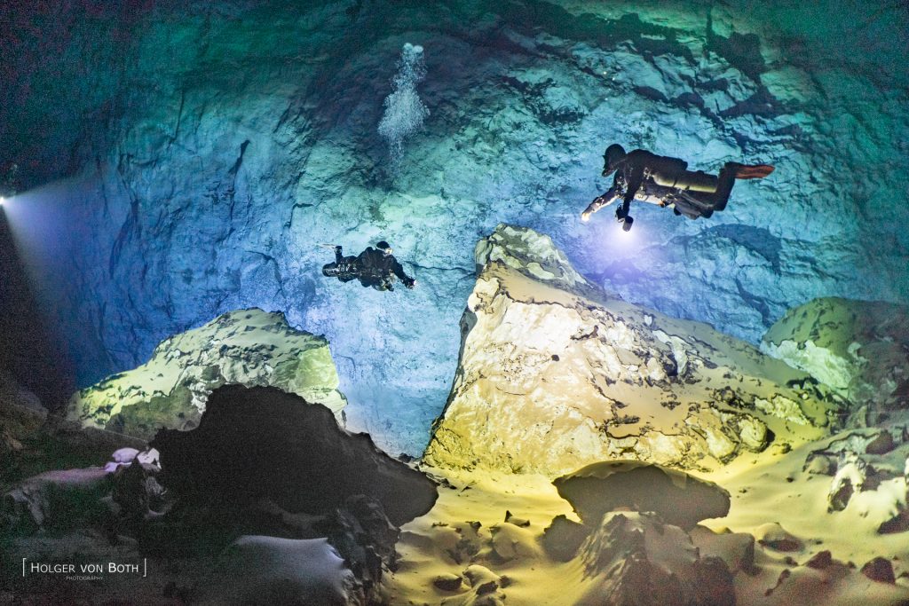 Two cave divers illuminating massive rock formations and a huge underwater cave wall inside Malazamanga Cave in Madagascar.