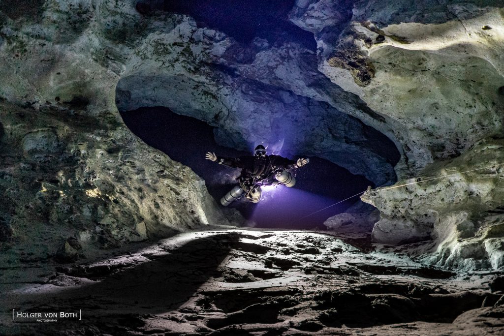Technical cave diver passing between illuminated white chambers inside Anjanamba Cave in Madagascar